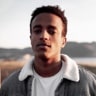 A young man with curly hair, wearing a grey jacket